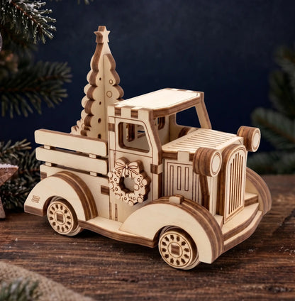 A wooden laser-cut Christmas truck ornament with a small Christmas tree in the bed, displayed on a rustic wooden surface with dark blue background and pine branches.