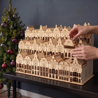 Hands remove small house drawer from tiered laser cut plywood Christmas village advent calendar beside holiday tree
