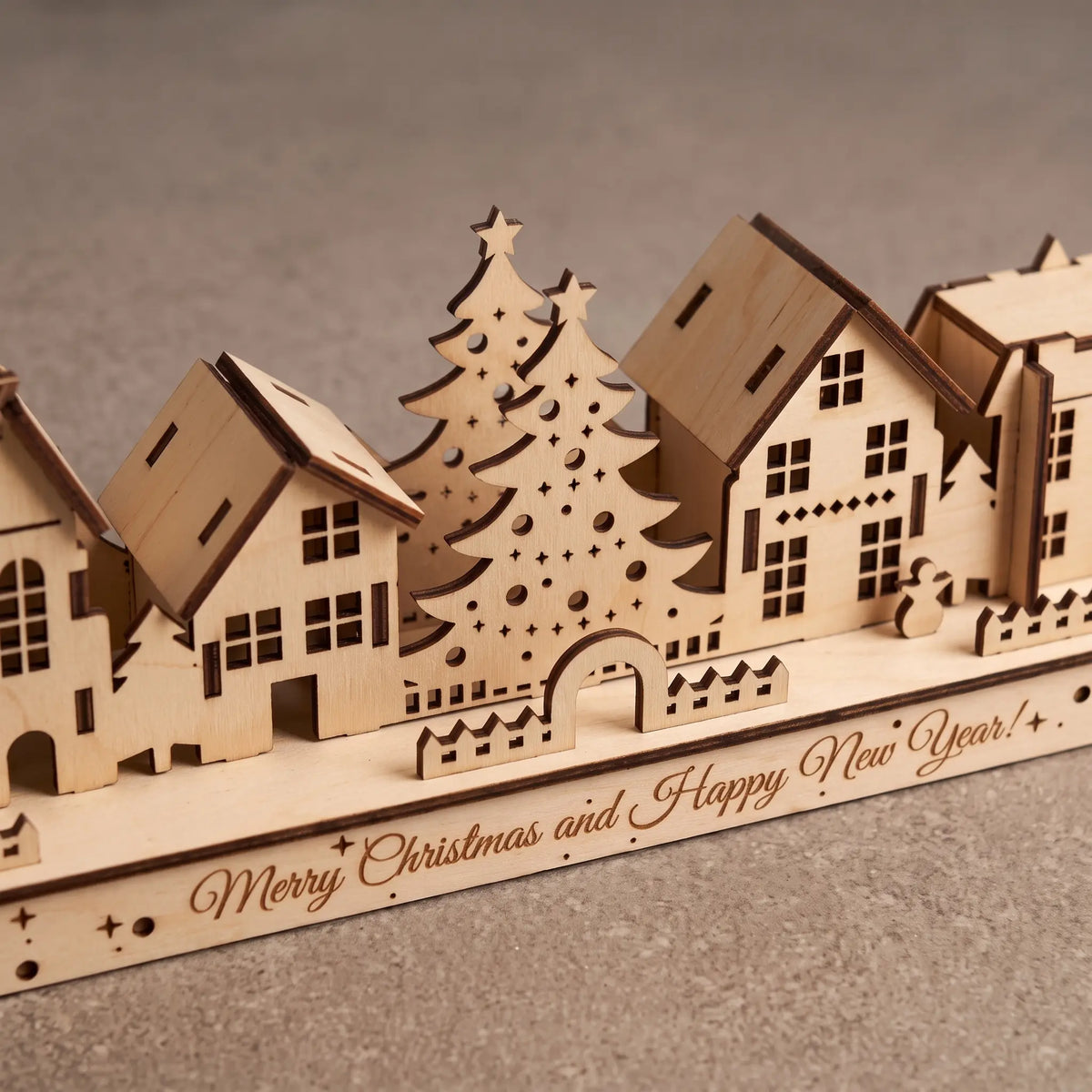 Close perspective of laser cut plywood holiday town houses and trees on engraved Happy New Year stand.