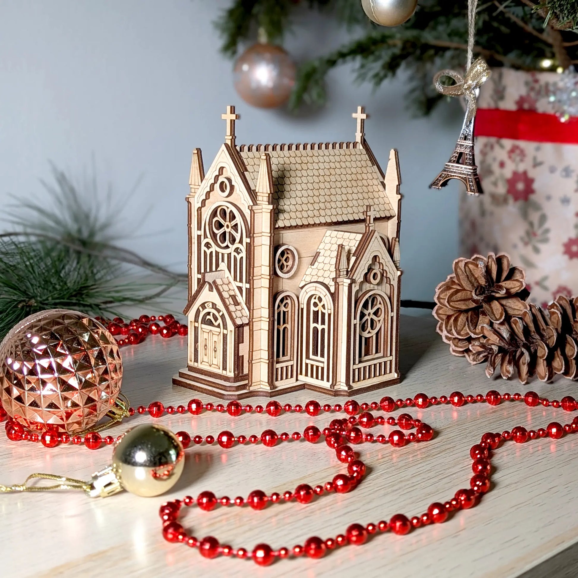 Alternate side view of a mini wooden church puzzle staged with holiday ornaments, crafted from layered laser cut plywood.