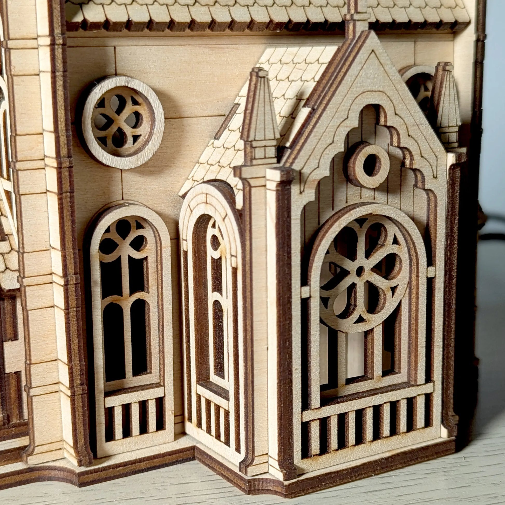 Macro close-up shot focusing on the delicate arched windows and gothic details of a mini laser cut plywood cathedral.