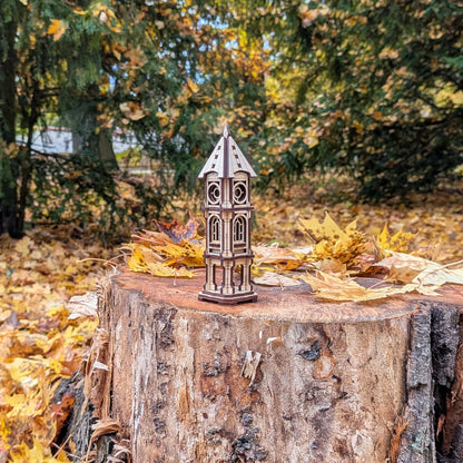 Wide scenic outdoor view of a miniature architectural clock tower model in laser cut plywood standing on a large tree stump