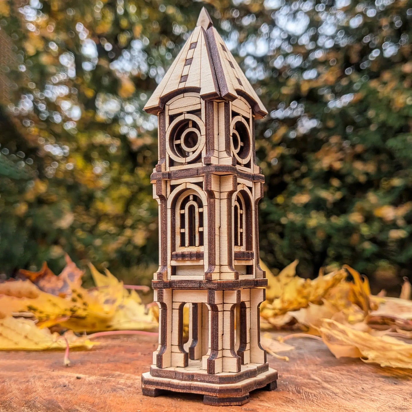 Low-angle scenic view of a detailed miniature architectural clock tower model made of laser cut plywood with forest bokeh