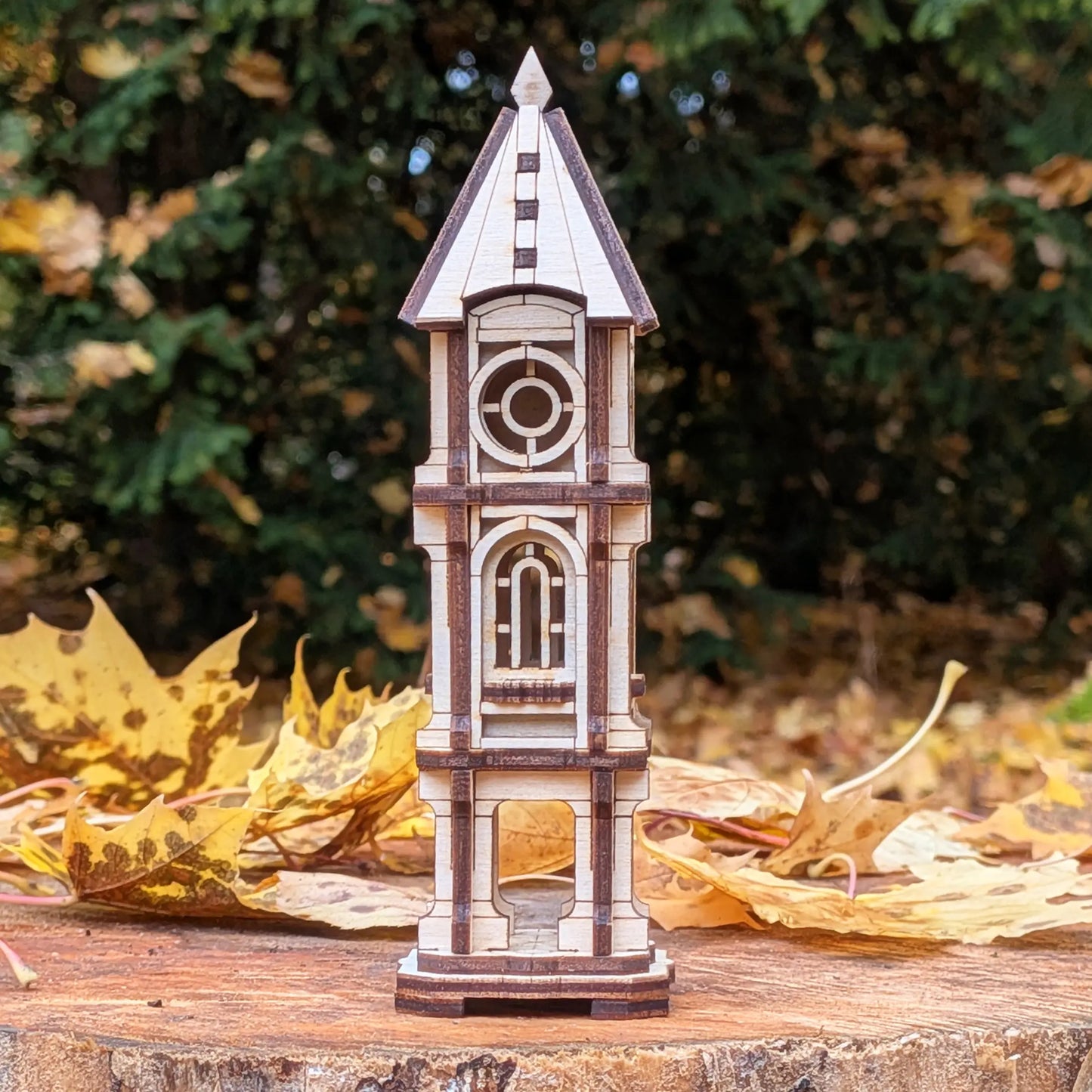 Eye-level straight shot of a miniature architectural clock tower model made of laser cut plywood on an autumn wood stump