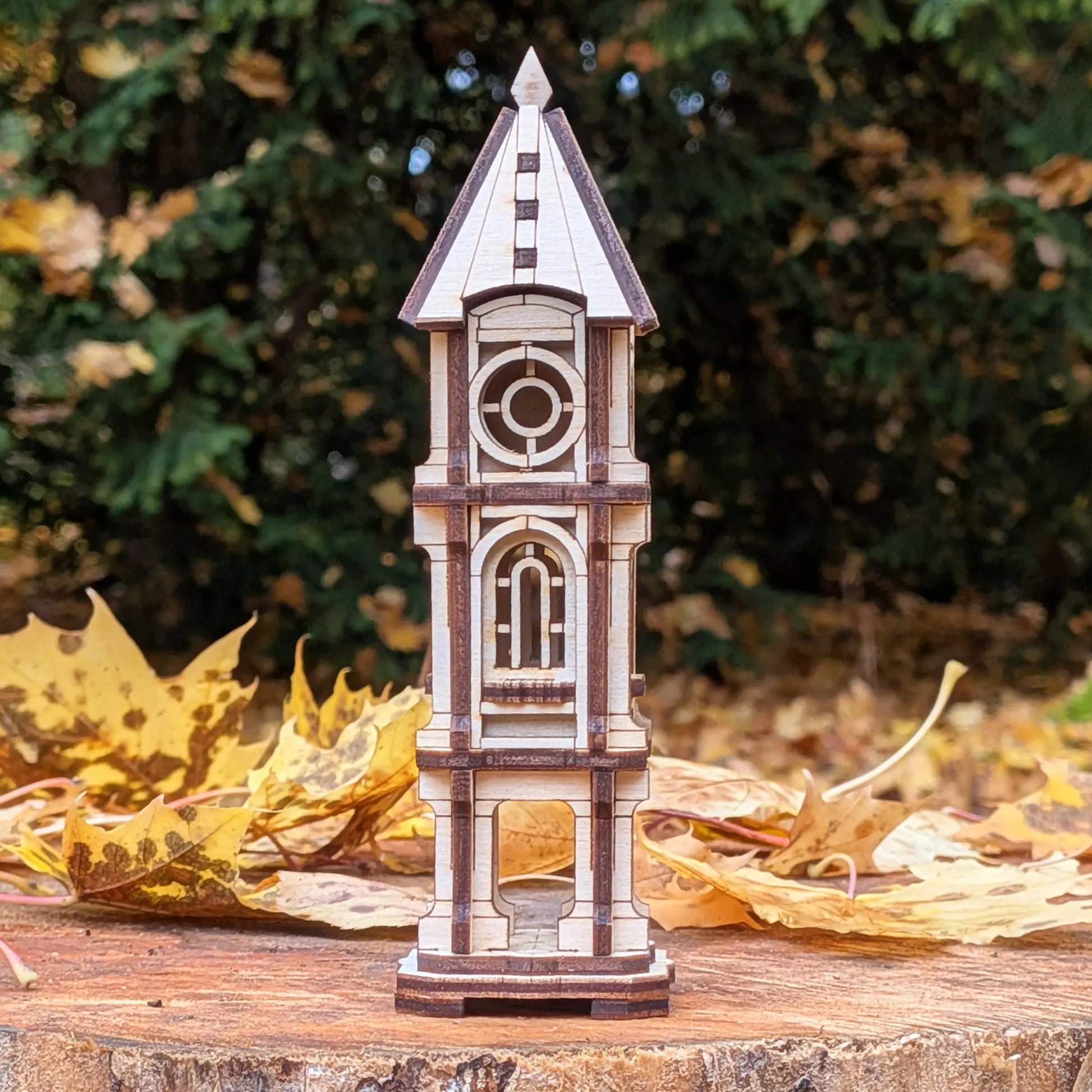 Eye-level straight shot of a miniature architectural clock tower model made of laser cut plywood on an autumn wood stump