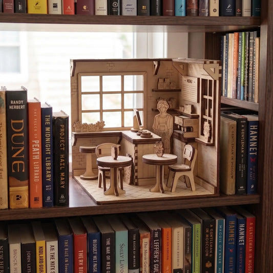 Miniature model of a cafe with furniture on a bookshelf surrounded by books