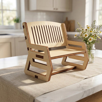 Detailed view of a miniature laser cut plywood bench with a wide seat and multiple vertical back slats. The dark, scorched edges of the wood create a striking contrast against the light birch tone. A small jar of daisies sits in the background.