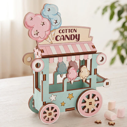 Painted pastel laser cut plywood cotton candy cart miniature with striped canopy and marshmallows on white wooden table.