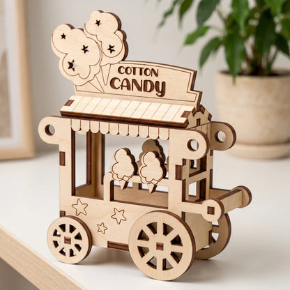 Natural laser cut plywood cotton candy cart miniature standing on white table next to a potted green houseplant in blur.