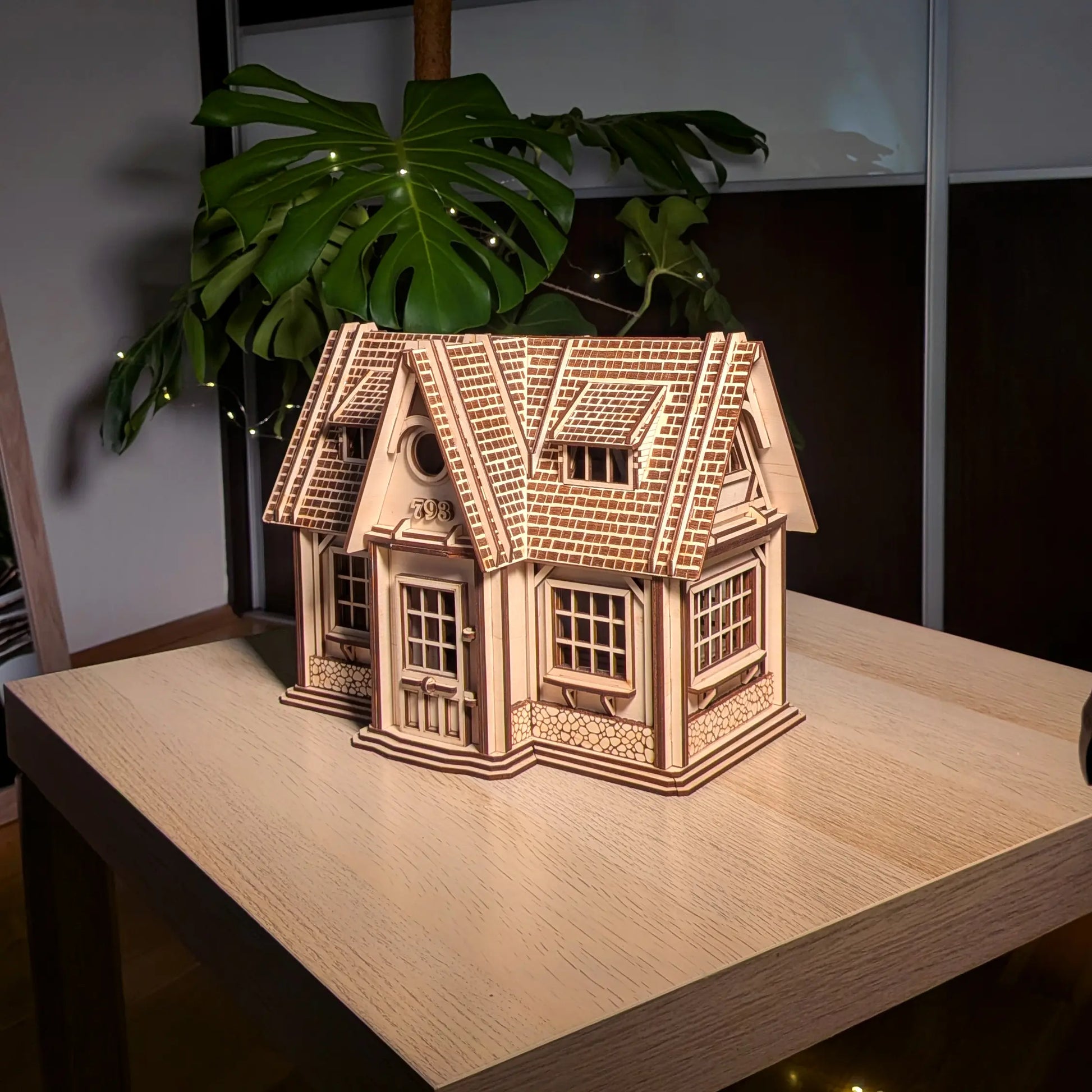 Full front view of a finished laser cut plywood country house model with a detailed shingle roof, set on a light wood table.