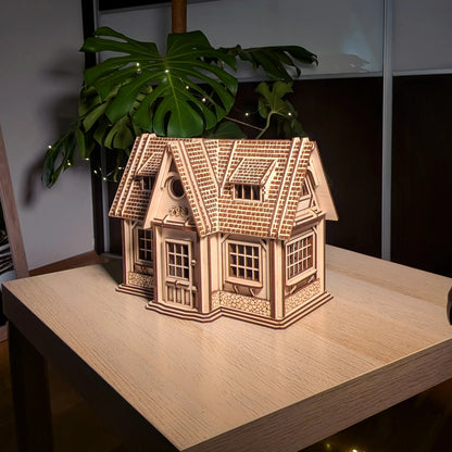 Full front view of a finished laser cut plywood country house model with a detailed shingle roof, set on a light wood table.