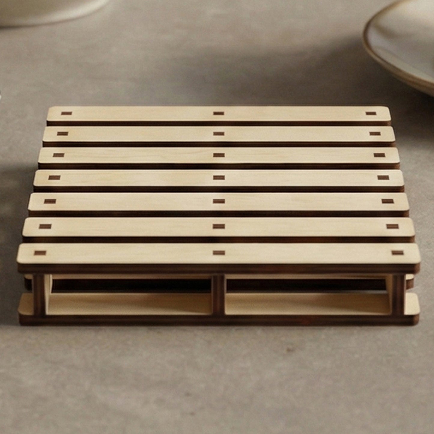 Laser cut wooden cup holder designed as a mini pallet, with slatted top and sturdy base, placed on a cozy kitchen countertop background.