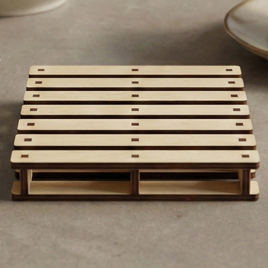 Laser cut wooden cup holder designed as a mini pallet, with slatted top and sturdy base, placed on a cozy kitchen countertop background.