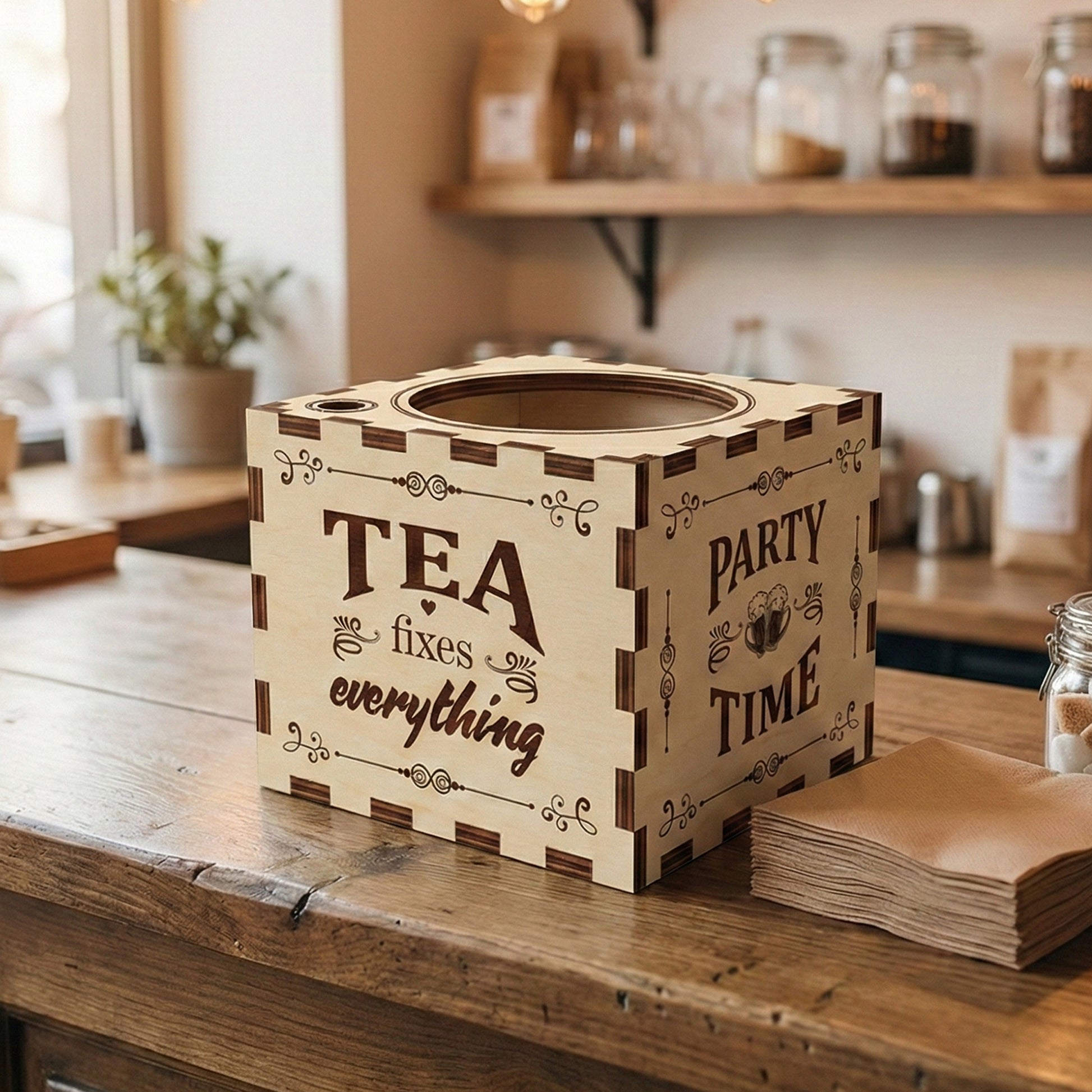 Empty laser cut plywood cup holder box on a wooden bar. Close-up on the dark scorched finger-joint corners and the engraved "PARTY TIME" and "TEA fixes everything" typography. Large circular cutout on top for cup storage.