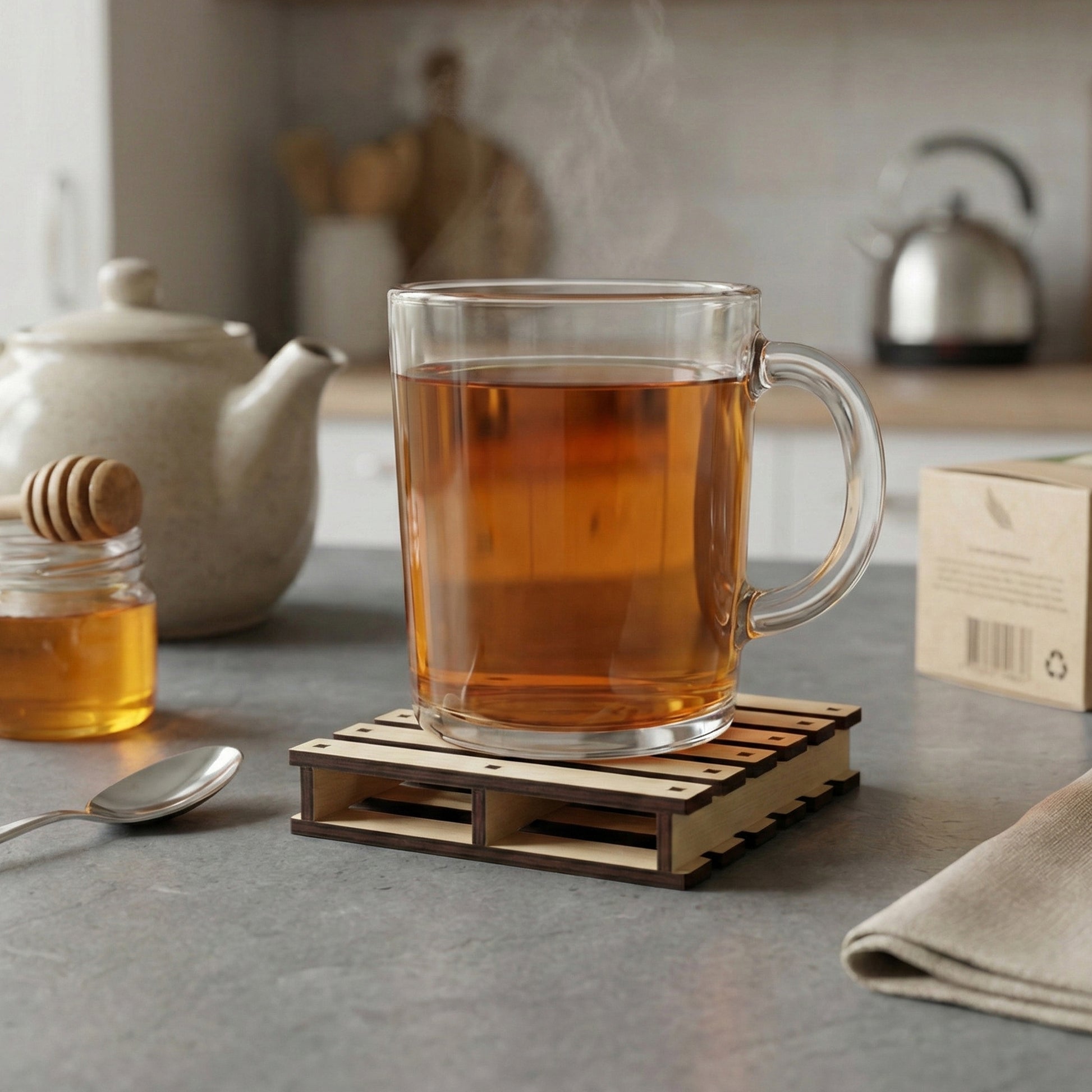 Laser cut wooden pallet cup holder in beige tones supporting a steaming glass of tea, on a soft kitchen table background.