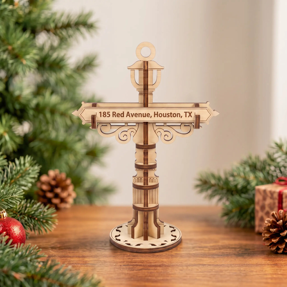 Laser cut plywood custom street signpost ornament on wooden table in front of Christmas tree with pine cones and gift box