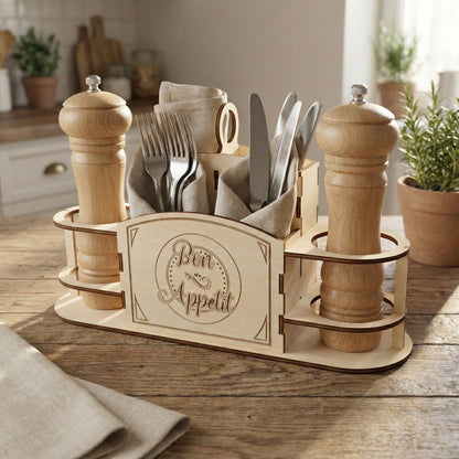 Laser cut plywood cutlery and spice caddy on a wooden table. Front panel features an etched "Bon Appetit" design. Side rings hold two large wooden pepper grinders. Central compartments are filled with silverware and linen napkins.