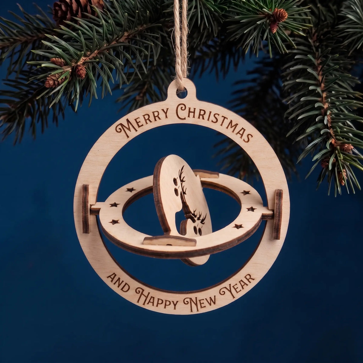 3D kinetic laser cut plywood bauble with spinning deer disc and holiday greetings hanging on pine branch on blue.