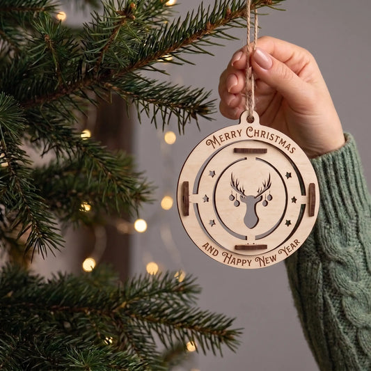 Hand holds hanging laser cut plywood stag bauble ornament showing true scale near illuminated pine tree boughs.