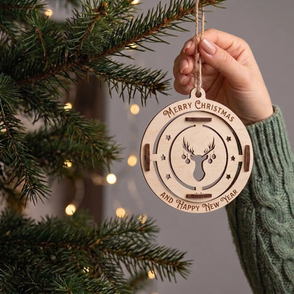 Hand holds hanging laser cut plywood stag bauble ornament showing true scale near illuminated pine tree boughs.