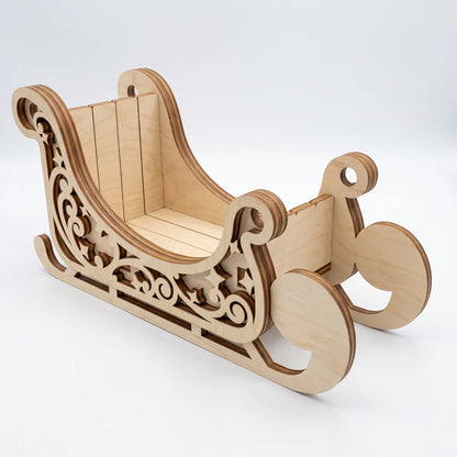Perspective view of unpainted laser cut plywood Santa sleigh model with cutout side scrolls on plain white