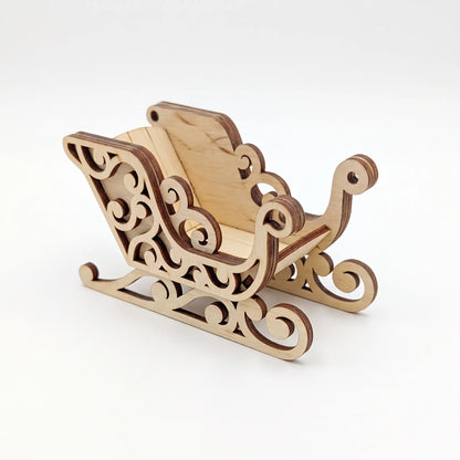 Front angle view of compact laser cut plywood Santa sleigh ornament with cutout swirls on white backdrop.