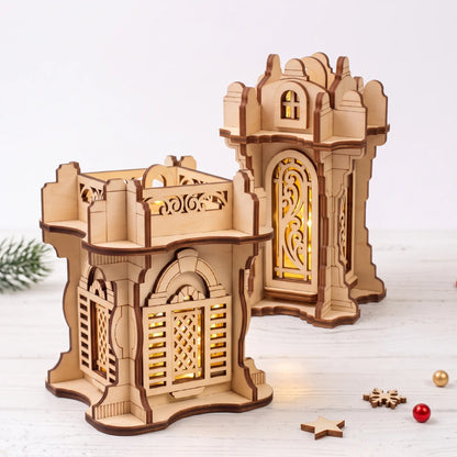 Pair of glowing laser cut plywood lanterns with arched fretwork windows on white wooden table with holiday decorations.
