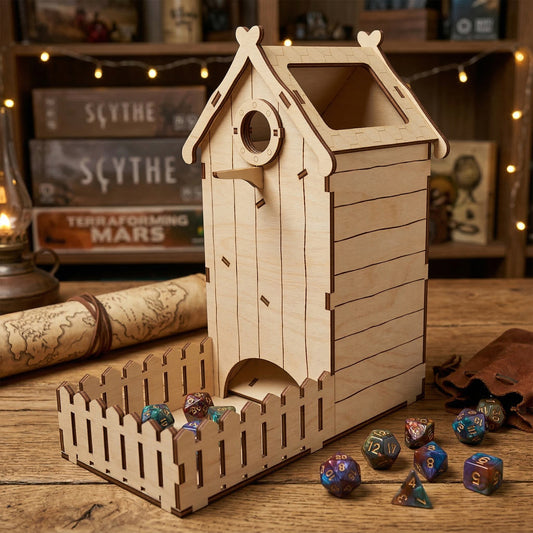 Birdhouse-style dice tower made of laser cut plywood with an etched shingle roof and a picket fence tray. Colorful polyhedral dice rest inside the wooden landing area. Set on a rustic table with board games and a scroll in the background.