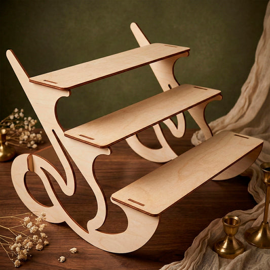 Laser cut wooden plywood display stand with 3 tiers features elegant curved scroll sides and slot assembly. Empty light wood retail riser sits on a dark wooden table with dried flowers and brass decor, showcasing the plywood construction and tiered design for craft show setups.