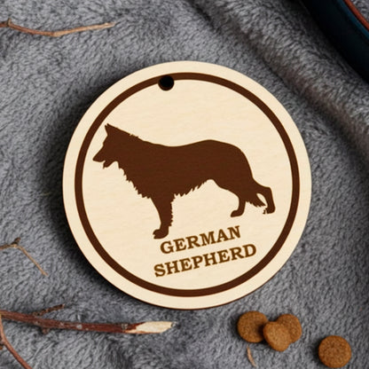 Laser cut wooden plywood dog tag  featuring an engraved black silhouette and breed name on a light wood round charm. The tag is displayed on a soft gray blanket next to a dark blue leather collar, dried sticks, and dog kibble, showing its use as a pet ID or gift