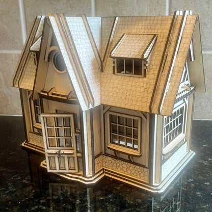 Front view photo of an assembled laser cut plywood country house model with an open entry door on a shiny dark surface.
