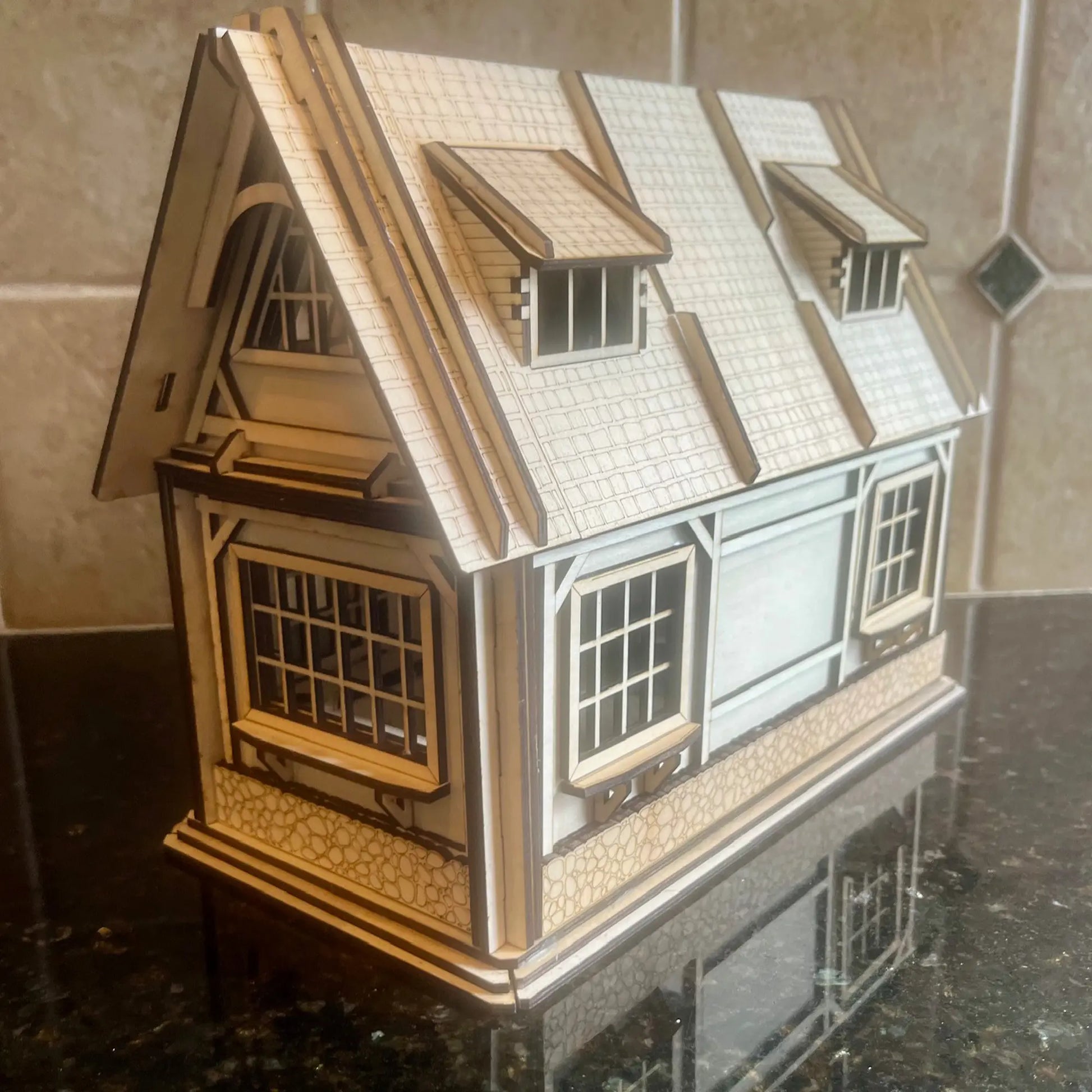 Side profile photo of a real laser cut plywood miniature house featuring dormer windows and detailed shingle roofing.