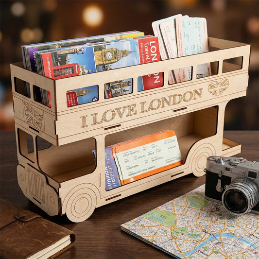 Laser cut plywood London bus postcard holder shown at an angle. Top and bottom decks are filled with travel brochures and tickets. Displayed next to a vintage camera and map to show scale and travel theme.