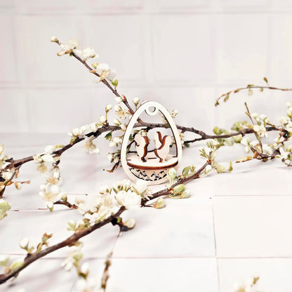 Laser cut plywood wooden Easter egg ornament featuring two chickens standing on a patterned base, framed by white blooming spring tree branches on a clean white background.