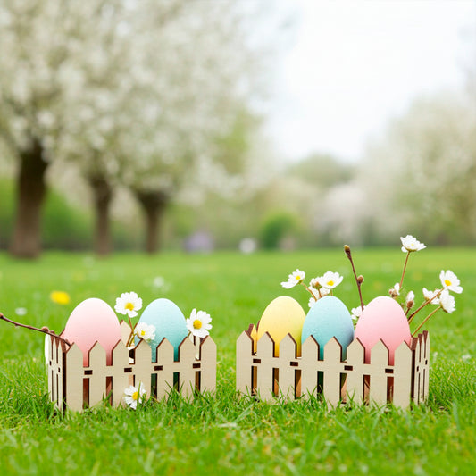 Two small laser cut plywood picket fence egg holders on bright green grass, each containing three pastel-colored Easter eggs and decorated with small white daisies.