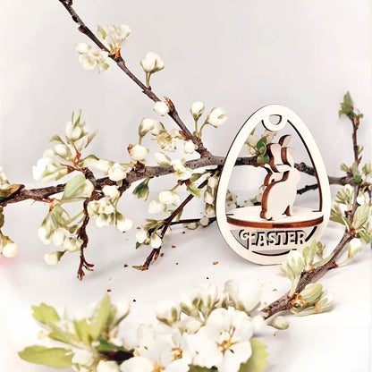 Laser cut plywood wooden Easter egg ornament with a detailed cutout of a playful bunny standing above the etched word "EASTER," framed by white blooming spring tree branches on a white background