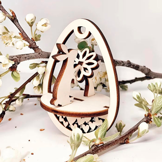 Laser cut  plywood wooden Easter egg ornament with a detailed cutout of a bunny holding a flower, framed by white blooming spring tree branches on a white background