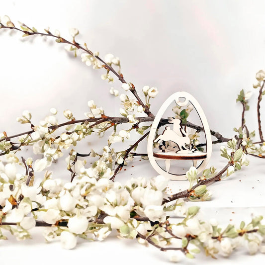 Laser cut plywood wooden Easter egg ornament with a detailed cutout of a bunny in motion, standing above a wooden base, framed by white blooming spring tree branches on a white background.