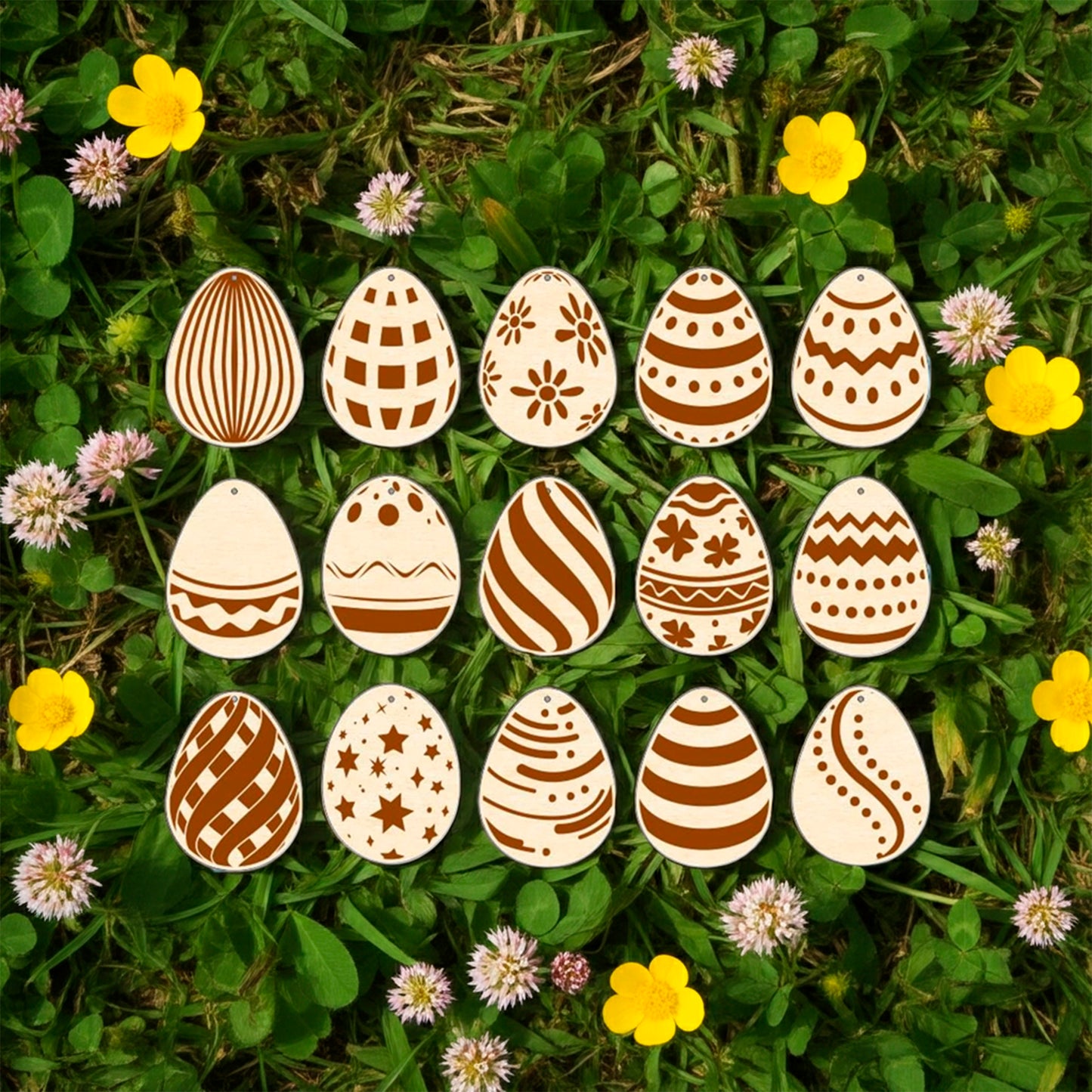 A set of fifteen light brown laser cut wooden plywood Easter egg ornaments, each engraved with a different geometric or floral pattern, lying on a bright green grass background among yellow buttercups and small pink flowers