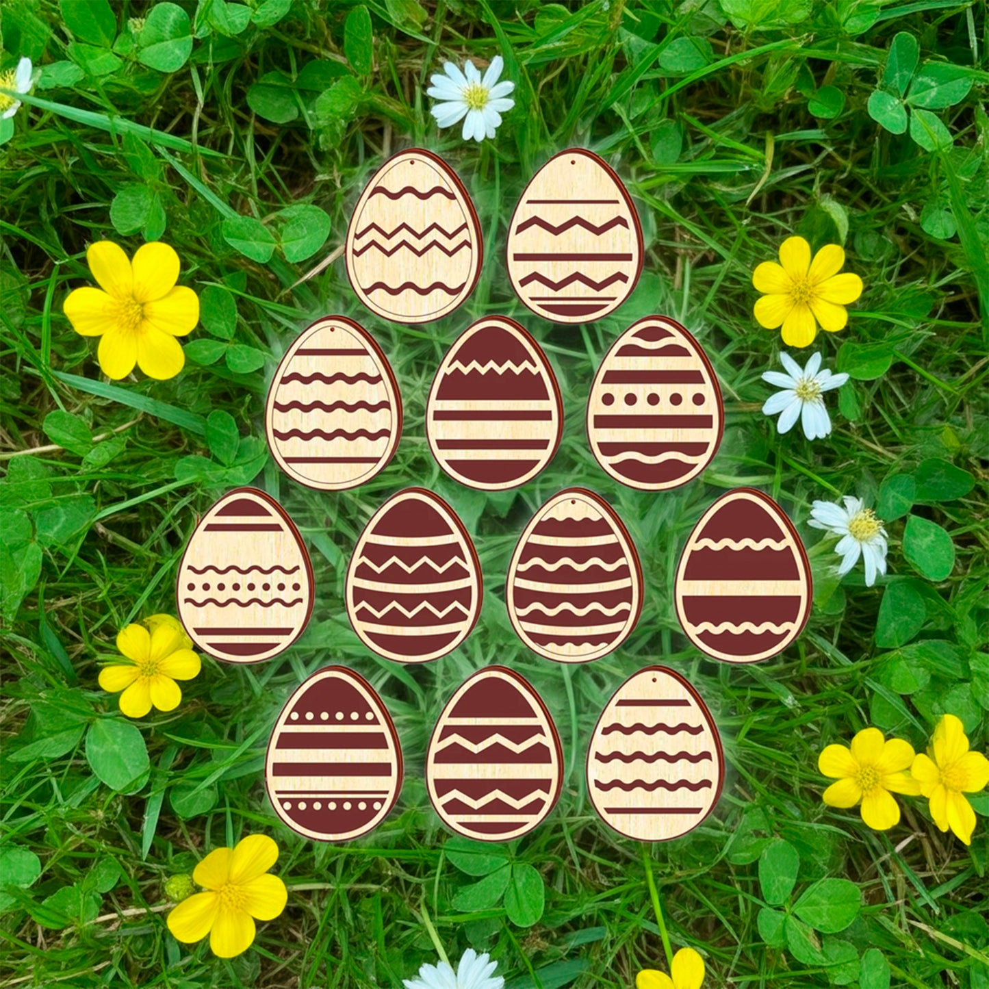 A set of twelve light brown laser cut wooden plywood Easter egg ornaments, each engraved with a different geometric or floral pattern, lying on a bright green grass background among yellow buttercups and small pink flowers