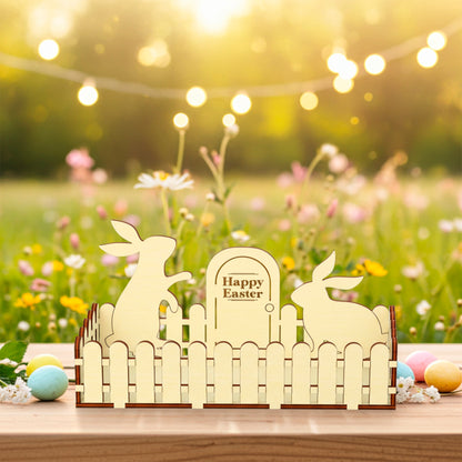 Laser cut  plywood wooden Easter fence decoration featuring two bunny silhouettes and a sign that reads "Happy Easter," styled outdoors on a table with colorful eggs and a wildflower background