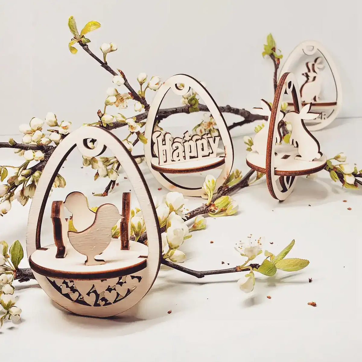 Wooden decorative laser cut easter ornaments on a white surface with branches and flowers.