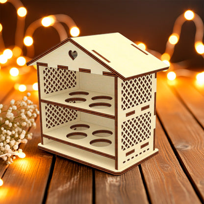 Laser cut plywood wooden house-shaped Easter egg holder with lattice sides and a heart cutout on the roof, featuring two shelves with four round slots each. It rests on a rustic wooden table with baby's breath flowers and warm, blurry fairy lights in the background.