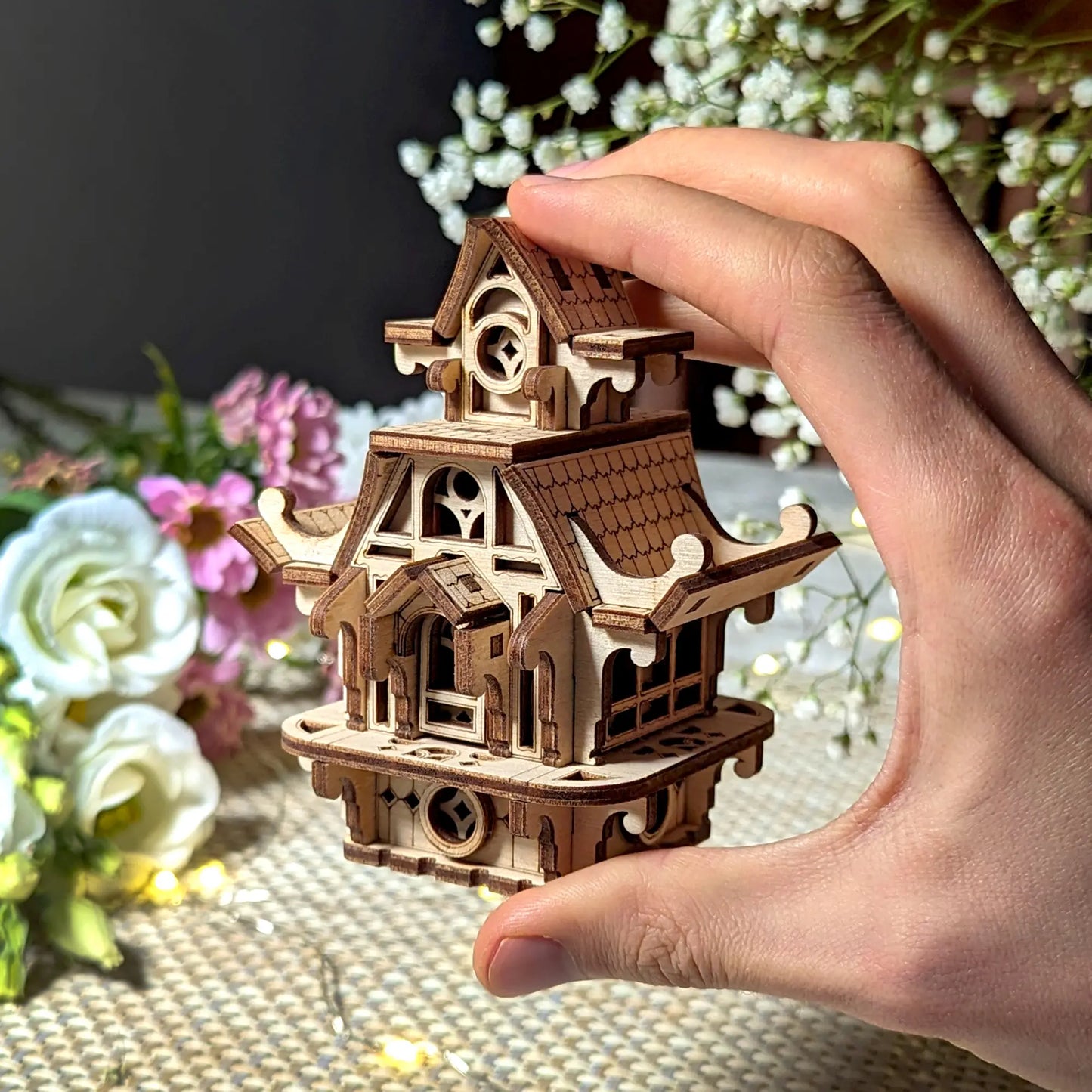 Hand holding a small laser cut plywood fairy house to show scale. Detailed wooden miniature home for collectors.