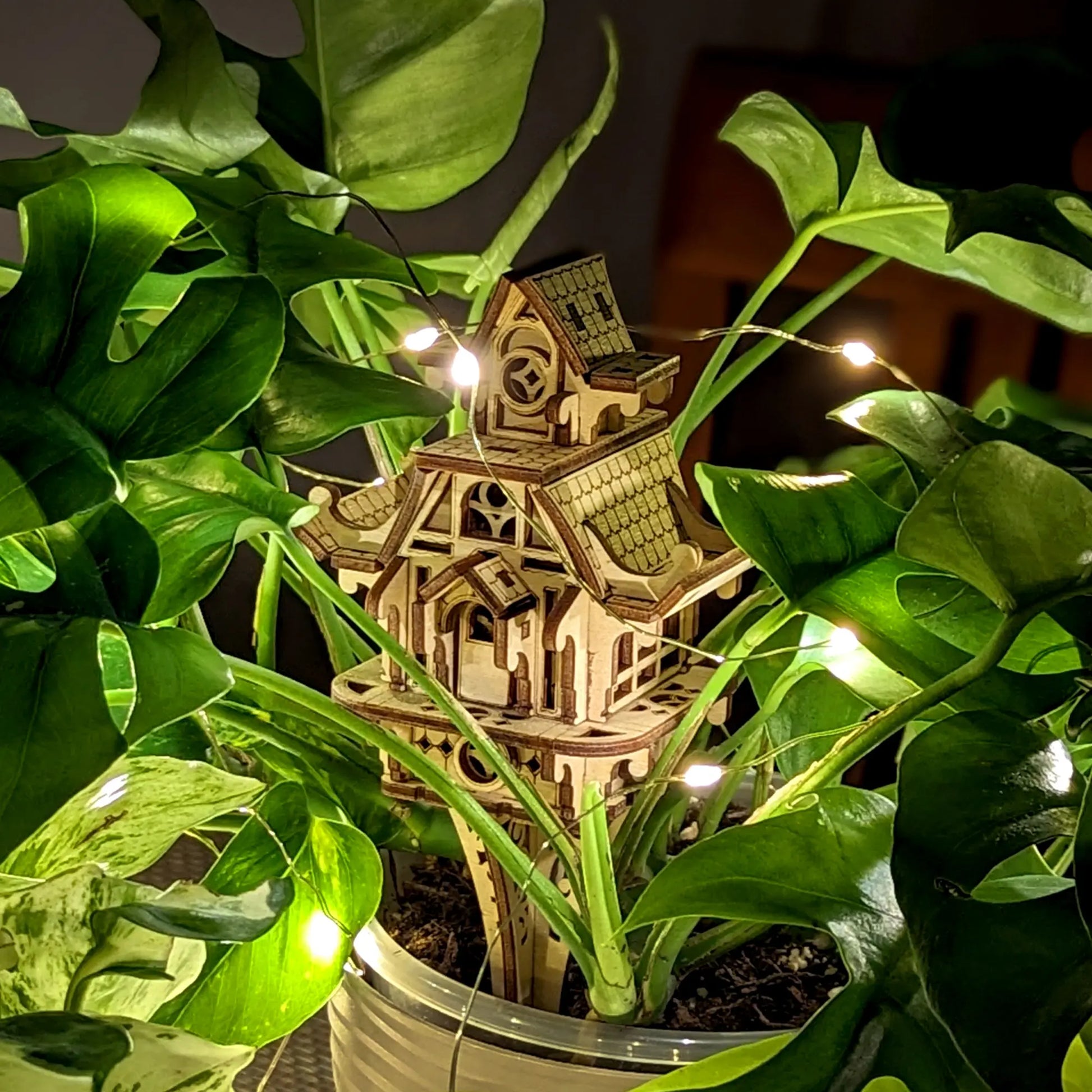 Laser cut plywood fairy house nestled in green leaves. Highlighting detailed wood texture and design.