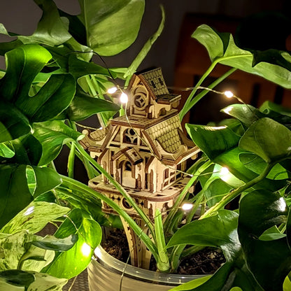 Laser cut plywood fairy house nestled in green leaves. Highlighting detailed wood texture and design.