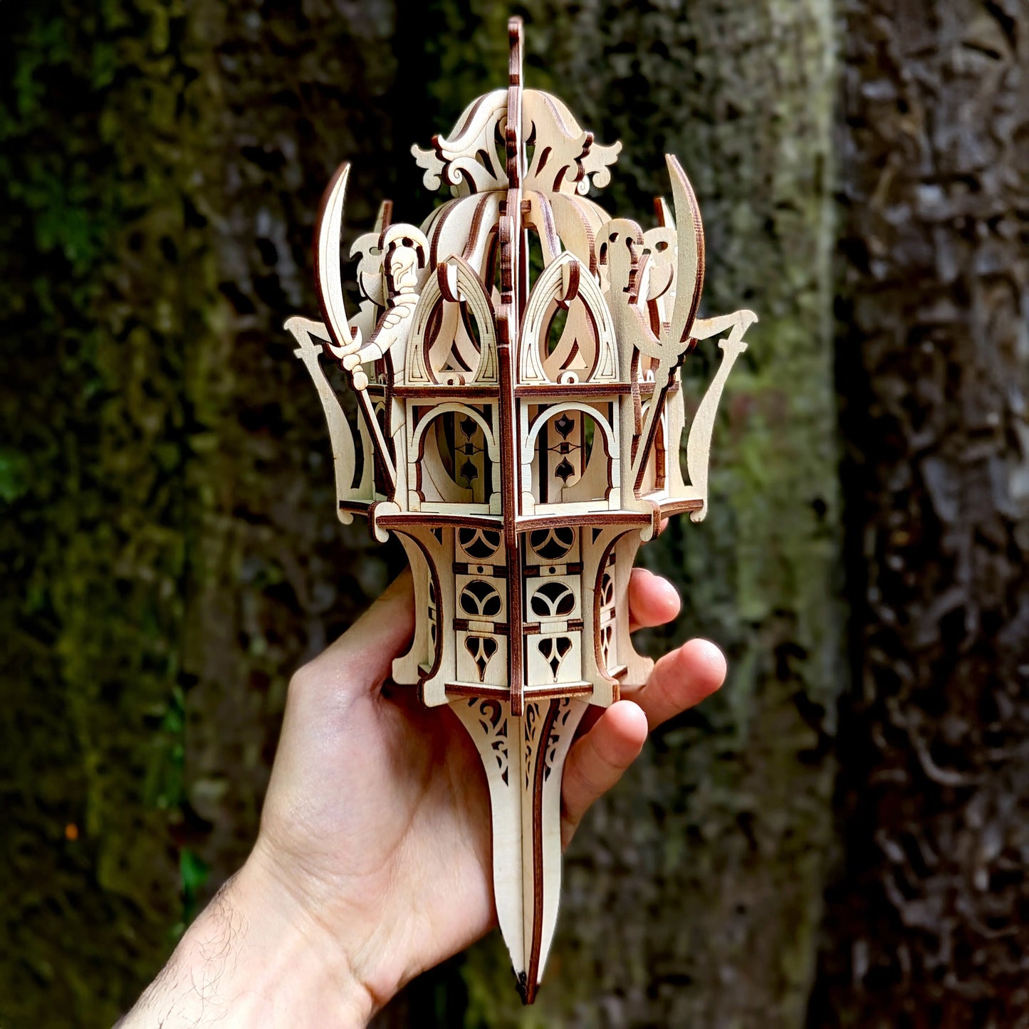 Detailed close-up of a laser cut plywood fantasy tower held in a male hand, showing fine engravings and layered design.