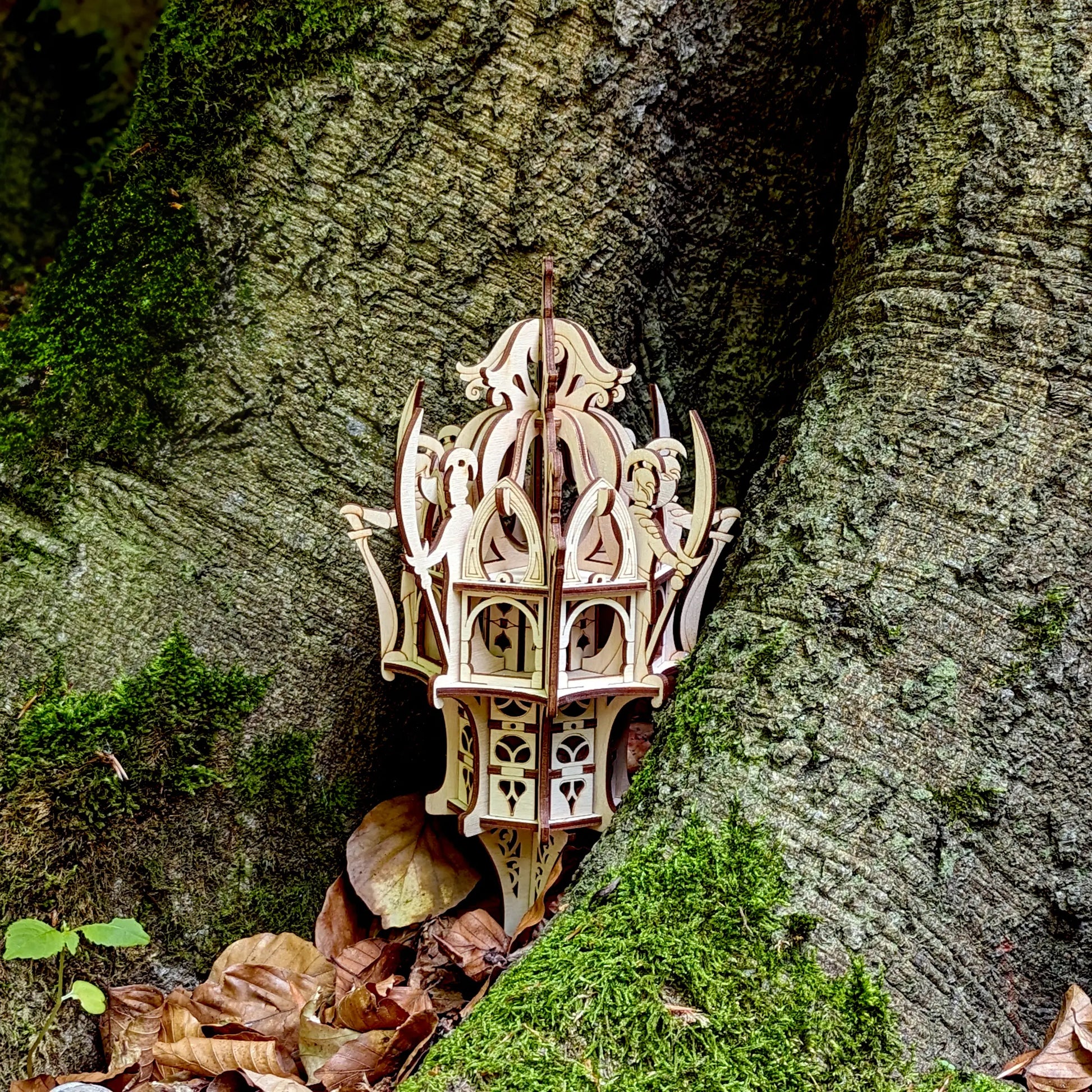 Medium shot of an intricate laser cut plywood elven dice tower lantern standing in a hollow root with dry autumn leaves.