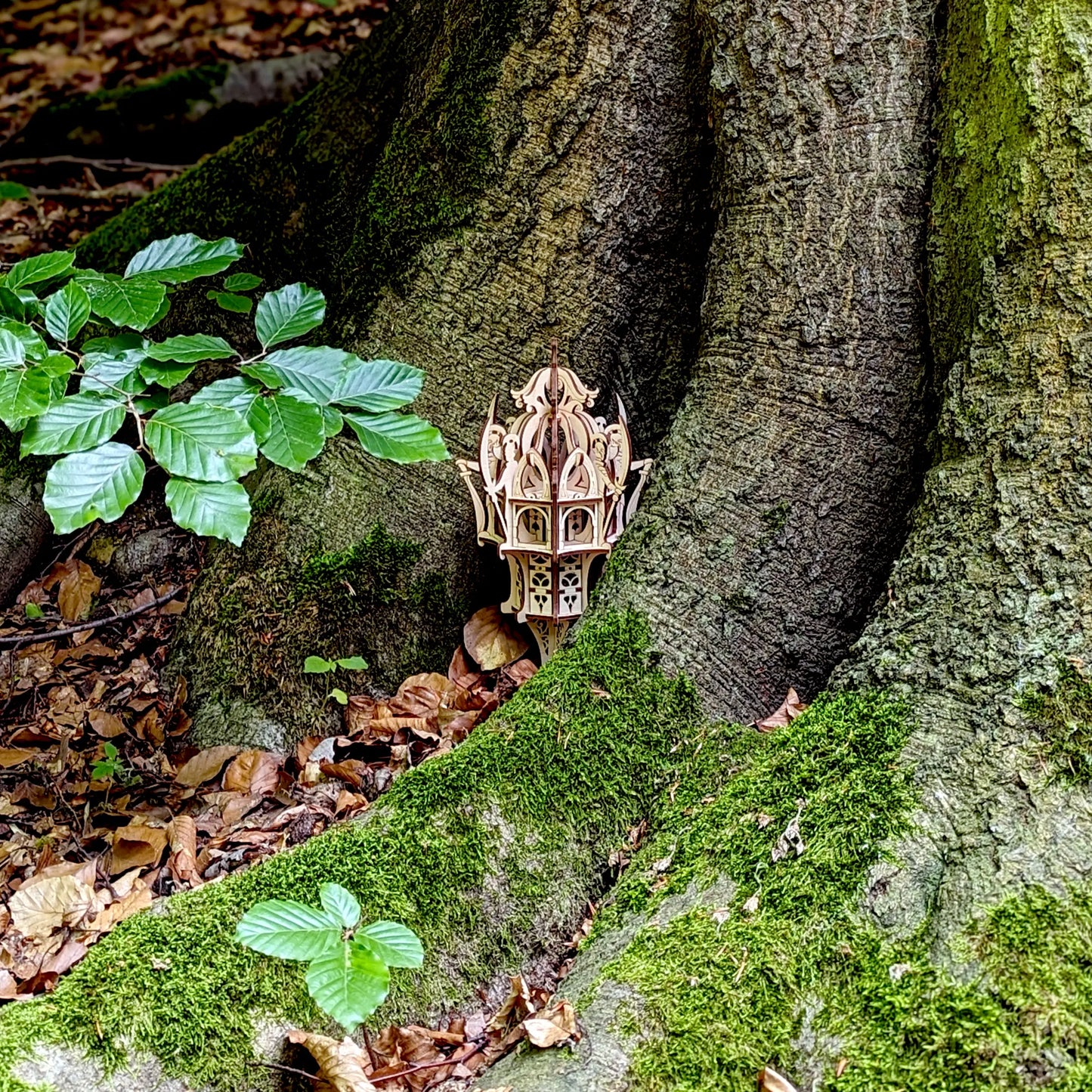 Distant view of a small laser cut plywood mystical castle tower hidden inside a large ancient tree root with green leaves.