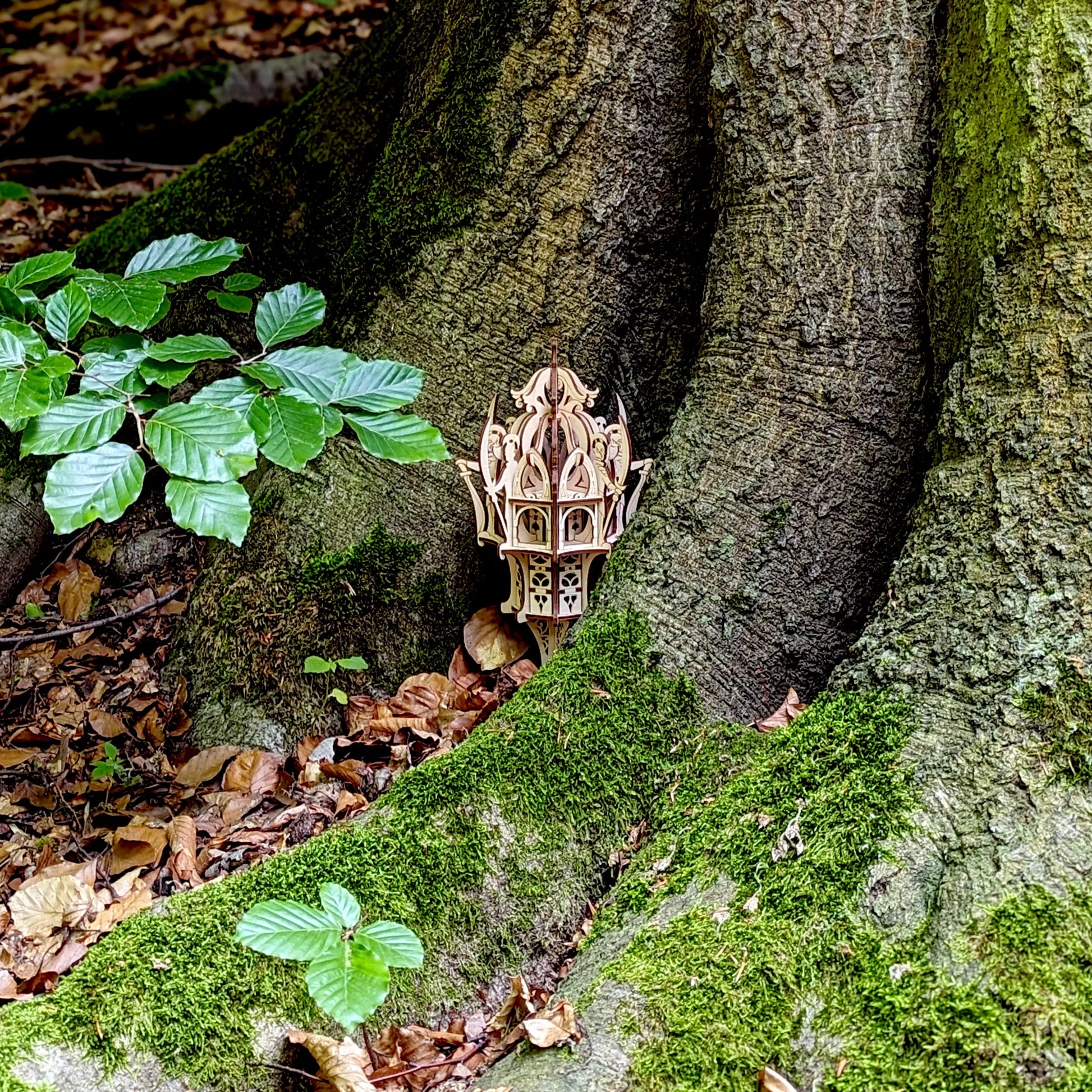 Distant view of a small laser cut plywood mystical castle tower hidden inside a large ancient tree root with green leaves.